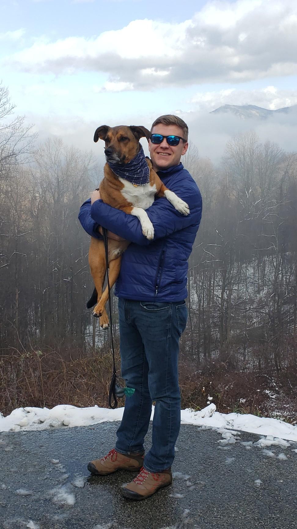 Nathaniel Abbott, holding his dog, Renly, with mountains in the background.